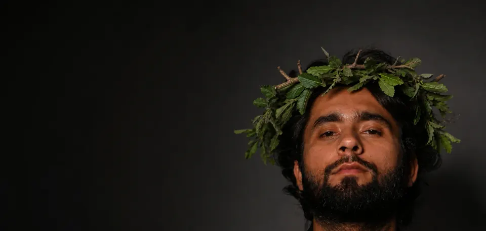 Cinematic portrait of a man wearing a leafy crown against a dark background